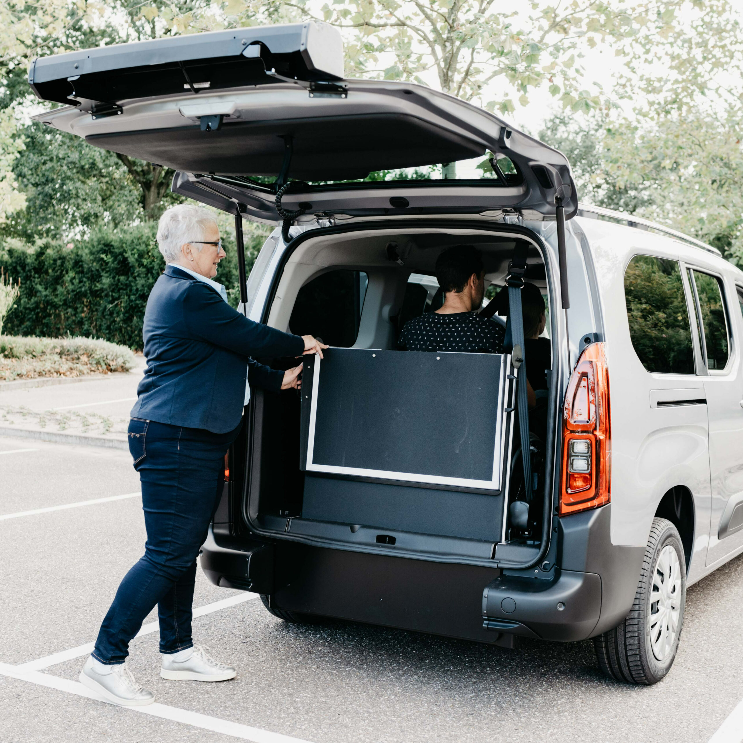 Femme Rampe Acces Fauteuil Roulant Vehicule Adapte Femme utilisant une rampe d'accès pour fauteuil roulant dans un véhicule adapté gris clair.