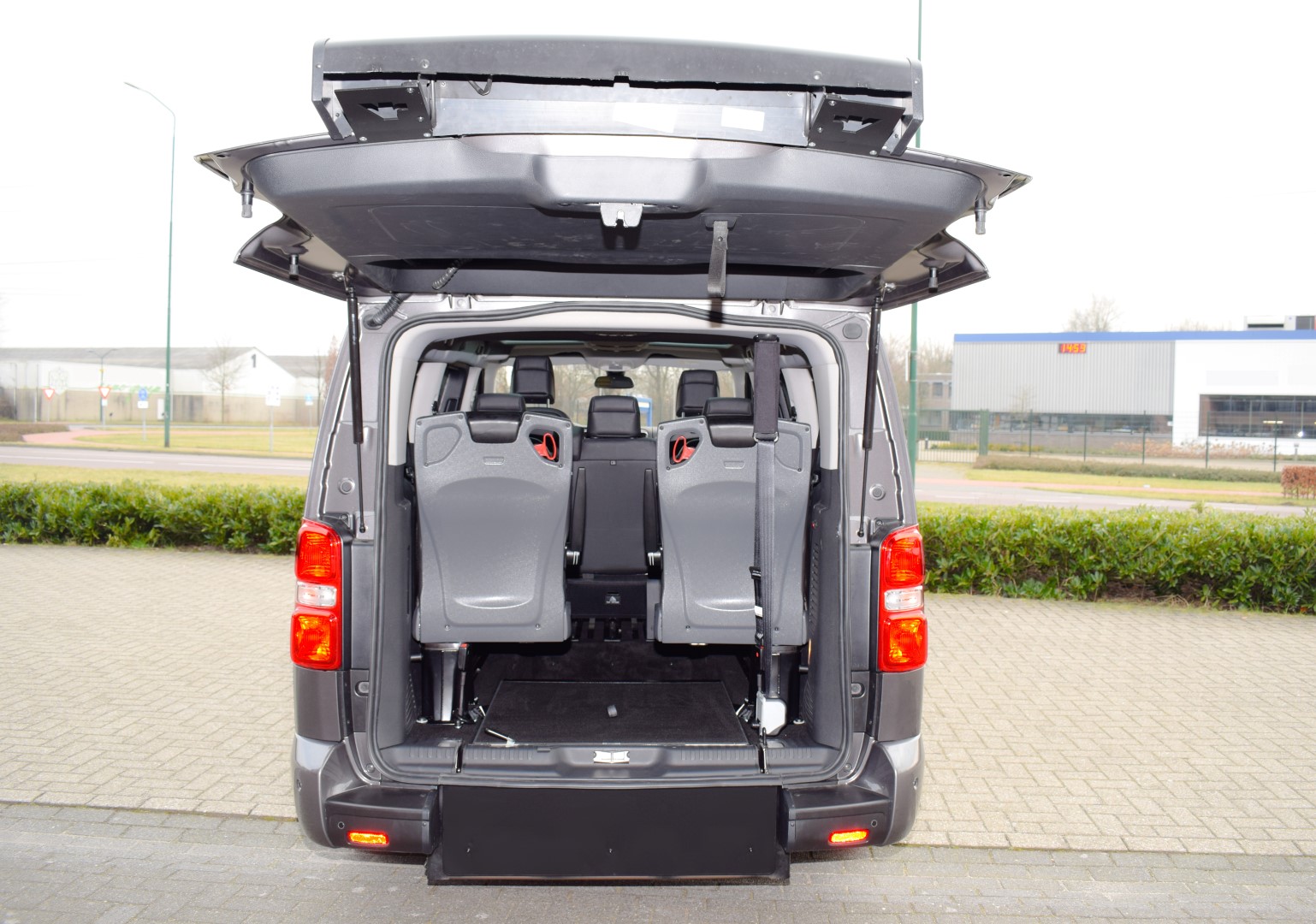 Citroen-Jumpy-TPMR Intérieur d'un monospace gris avec hayon ouvert et sièges rabattables. Véhicule aménagé pour personnes à mobilité réduite.