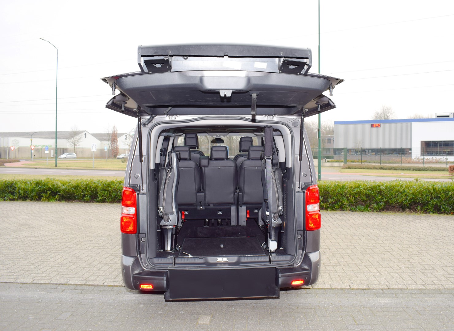 Citroen-Jumpy-TPMR Intérieur d'un van gris avec hayon ouvert et rampe d'accès pour fauteuil roulant. Sièges noirs visibles.
